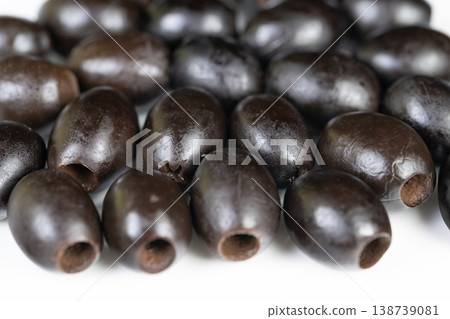 Row of pitted black olives lined on white plane, hollow centers clearly visible, studiolit still life conveying garnish idea, antipasto mood, preserved ingredient ready for plating 138739081