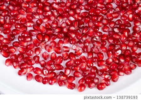 Bright pomegranate seeds on white plate, chef garnish concept, glossy ruby arils spread in minimalist composition, highkey lighting emphasizes freshness and juicy texture Bright pomegranate seeds on white plate, chef garnish concept, glossy ruby arils spread in minimalist composition, highkey lighting emphasizes freshness and juicy texture 138739193
