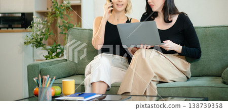 Two women collaborating on a project at home, brainstorming with a laptop and notebook in a cozy setting. 138739358