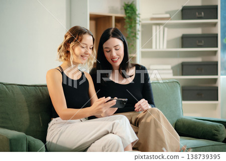 Two women collaborating on a project at home, brainstorming with a laptop and notebook in a cozy setting. Two women collaborating on a project at home, brainstorming with a laptop and notebook in a cozy setting. 138739395
