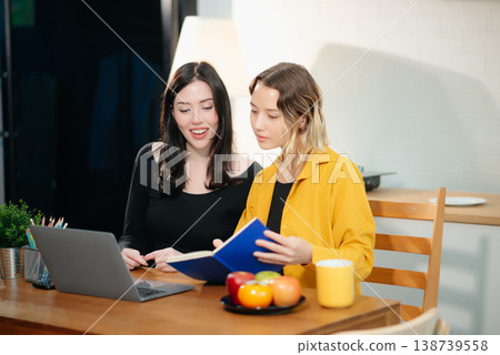 Two professional women collaborating on a business project with a laptop, notebook, and coffee at home. 138739558
