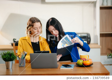 Two professional women collaborating on a business project with a laptop, notebook, and coffee at home. Two professional women collaborating on a business project with a laptop, notebook, and coffee at home. 138739589