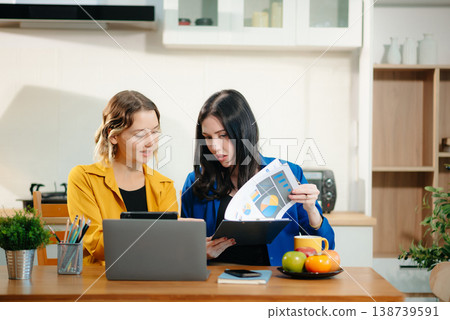Two professional women collaborating on a business project with a laptop, notebook, and coffee at home. Two professional women collaborating on a business project with a laptop, notebook, and coffee at home. 138739591