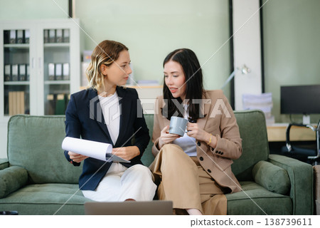 Two women collaborating on a project on sofa at home, brainstorming with a laptop and notebook Two women collaborating on a project on sofa at home, brainstorming with a laptop and notebook 138739611