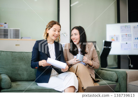 Two women collaborating on a project on sofa at home, brainstorming with a laptop and notebook Two women collaborating on a project on sofa at home, brainstorming with a laptop and notebook 138739613