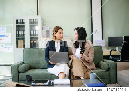 Two women collaborating on a project on sofa at home, brainstorming with a laptop and notebook Two women collaborating on a project on sofa at home, brainstorming with a laptop and notebook 138739614