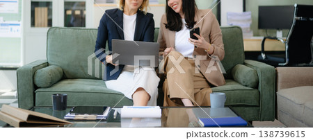 Two women collaborating on a project on sofa at home, brainstorming with a laptop and notebook 138739615