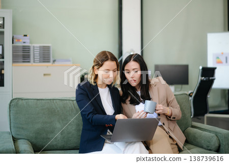 Two women collaborating on a project on sofa at home, brainstorming with a laptop and notebook 138739616