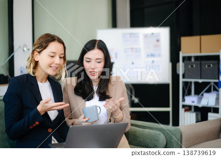 Two women collaborating on a project on sofa at home, brainstorming with a laptop and notebook Two women collaborating on a project on sofa at home, brainstorming with a laptop and notebook 138739619