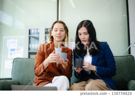 Two women collaborating on a project on sofa at home, brainstorming with a laptop and notebook Two women collaborating on a project on sofa at home, brainstorming with a laptop and notebook 138739820