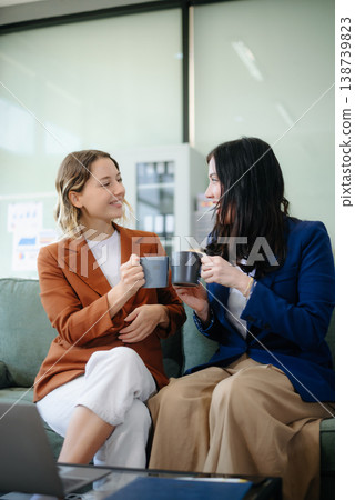 Two women collaborating on a project on sofa at home, brainstorming with a laptop and notebook Two women collaborating on a project on sofa at home, brainstorming with a laptop and notebook 138739823