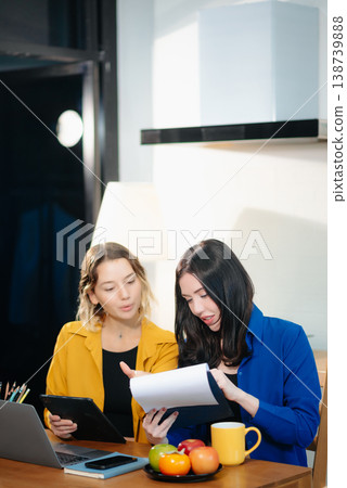 Two professional women collaborating on a business project with a laptop, notebook, and coffee at home. 138739888