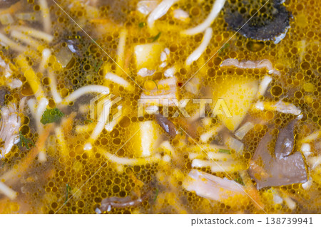 Closeup homemade mushroom soup glistening with golden oil droplets, soft noodles, mushroom pieces and diced root vegetable, mealprep friendly comfort ready for storage 138739941