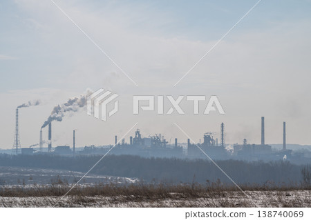 Metallurgical plant on distant horizon at dawn, soft early light and rising vapor, cooling towers and cranes creating silhouettes, snowy foreground and tranquil industrial mood 138740069