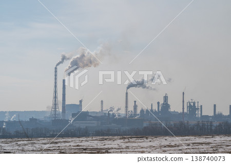 Factories belch smoke across snowy plains landscape. Metallurgical industrial complex emitting thick smoke over snowy terrain with distant structures and pipelines Factories belch smoke across snowy plains landscape. Metallurgical industrial complex emitting thick smoke over snowy terrain with distant structures and pipelines 138740073