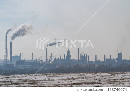 Factories belching smoke over fields. Lazy clouds fade behind distant refinery structures. Muted gray sky over desolate industrial landscape signifies environmental worries 138740074