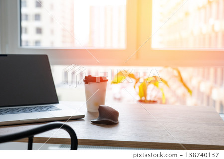A cup of coffee, a laptop with graphics and charts printed on paper, lying on a windowsill near a window of an apartment. The concept of remote work. 138740137