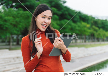 Young woman smiles, holding tablet outdoors Young woman smiles, holding tablet outdoors 138742230