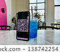 Smartphone displaying a QR code for digital payment placed on a table next to a blue drink in a cafe. Cashless transaction, mobile banking, and contactless technology in modern lifestyle setting 138742254