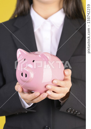A woman in a suit holding a piggy bank A woman in a suit holding a piggy bank 138742259