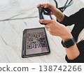 Close-up of a person using a smartphone to scan a QR code displayed on a tablet. Digital payment, mobile banking, and contactless transaction technology in modern lifestyle and fintech concept 138742266