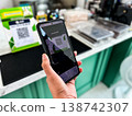 a person using a smartphone to scan a QR code for digital payment at a cafe counter. Modern cashless transaction, mobile banking, and contactless technology in everyday lifestyle 138742307