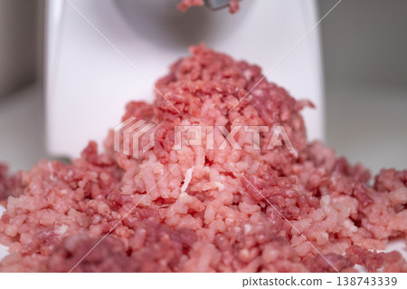 Close view of minced meat on counter. Unprocessed meat spilling from grinder during home cooking. Detailed view of fresh ground meat and juices on kitchen workspace 138743339