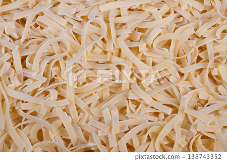 Uncooked egg noodles prepared. Closeup of dense egg noodle bundle in industrial setting. Massive quantity of uncooked egg noodles with dust on neutral industrial surface 138743352