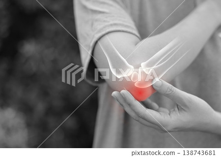 Monochrome photo of woman suffering from severe elbow pain, holding her arm with a red glowing anatomical bone graphic overlay showing joint inflammation, arthritis, or injury in medical concept. Monochrome photo of woman suffering from severe elbow pain, holding her arm with a red glowing anatomical bone graphic overlay showing joint inflammation, arthritis, or injury in medical concept. 138743681