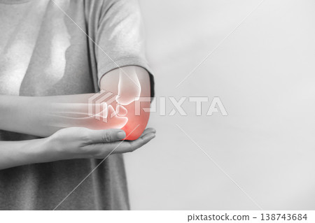 Monochrome photo of woman suffering from severe elbow pain, holding her arm with a red glowing anatomical bone graphic overlay showing joint inflammation, arthritis, or injury in medical concept. 138743684