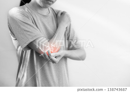 Monochrome photo of woman suffering from severe elbow pain, holding her arm with a red glowing anatomical bone graphic overlay showing joint inflammation, arthritis, or injury in medical concept. Monochrome photo of woman suffering from severe elbow pain, holding her arm with a red glowing anatomical bone graphic overlay showing joint inflammation, arthritis, or injury in medical concept. 138743687