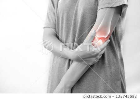Monochrome photo of woman suffering from severe elbow pain, holding her arm with a red glowing anatomical bone graphic overlay showing joint inflammation, arthritis, or injury in medical concept. 138743688