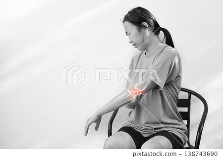 Monochrome photo of woman suffering from severe elbow pain, holding her arm with a red glowing anatomical bone graphic overlay showing joint inflammation, arthritis, or injury in medical concept. Monochrome photo of woman suffering from severe elbow pain, holding her arm with a red glowing anatomical bone graphic overlay showing joint inflammation, arthritis, or injury in medical concept. 138743690