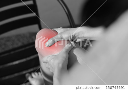 Close up monochrome photo of person hands holding painful knee with red glowing spot indicating severe joint pain, arthritis, sports injury, or inflammation in healthcare and medical concept. Close up monochrome photo of person hands holding painful knee with red glowing spot indicating severe joint pain, arthritis, sports injury, or inflammation in healthcare and medical concept. 138743691