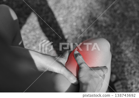 Close up monochrome photo of person hands holding painful knee with red glowing spot indicating severe joint pain, arthritis, sports injury, or inflammation in healthcare and medical concept. 138743692