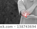 Monochrome photo of woman suffering from severe elbow pain, holding her arm with a red glowing anatomical bone graphic overlay showing joint inflammation, arthritis, or injury in medical concept. 138743694