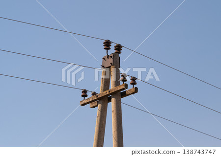 Pair of poles with electric lines, parallel conductors stretching across frame and creating rhythmic spacing against clear horizon, rural infrastructure composition 138743747