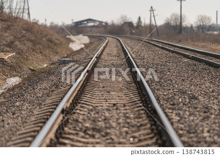 Horizon hides converging railway tracks. Silent sleepers and fasteners under cloudy overcast sky. Serene scene of railway ties and ballast fading into distant horizon Horizon hides converging railway tracks. Silent sleepers and fasteners under cloudy overcast sky. Serene scene of railway ties and ballast fading into distant horizon 138743815