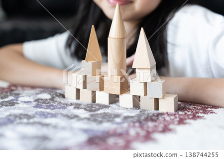 Natural wood blocks form small castle with three pointed towers as basic geometric pieces stand in ordered rows on soft fabric creating calm indoor play scene for spatial learning. Natural wood blocks form small castle with three pointed towers as basic geometric pieces stand in ordered rows on soft fabric creating calm indoor play scene for spatial learning. 138744255
