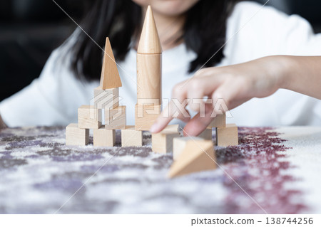 Natural wood blocks form small castle with three pointed towers as basic geometric pieces stand in ordered rows on soft fabric creating calm indoor play scene for spatial learning. 138744256