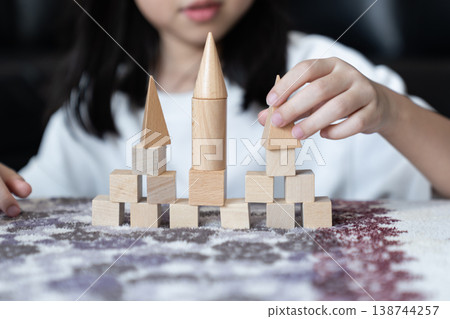 Natural wood blocks form small castle with three pointed towers as basic geometric pieces stand in ordered rows on soft fabric creating calm indoor play scene for spatial learning. 138744257