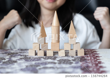 A child places wooden pieces with steady hands to complete the tower. The simple build suggests confidence, progress and self trust. A child places wooden pieces with steady hands to complete the tower. The simple build suggests confidence, progress and self trust. 138744264