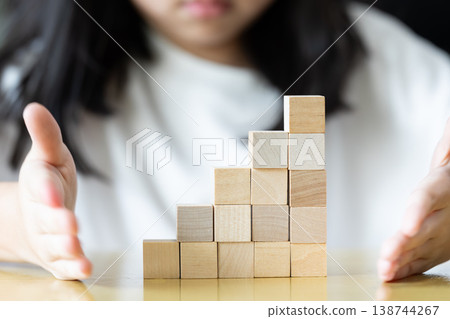 oth hands hold a wooden block tower as small fingers slowly adjust and place pieces one by one on a rug keeping the structure upright neat and stable through careful practice. 138744267