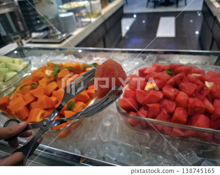 Candid Close-up of Hand Using Tongs to Pick Fresh Watermelon from Buffet Display Candid Close-up of Hand Using Tongs to Pick Fresh Watermelon from Buffet Display 138745165