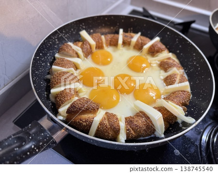 Eggs frying in pan surrounded by sesame bread and cheese, perfect for breakfast background Eggs frying in pan surrounded by sesame bread and cheese, perfect for breakfast background 138745540