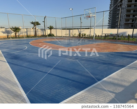 Outdoor basketball court with blue and orange surface under clear sky, ideal for sports background 138745564