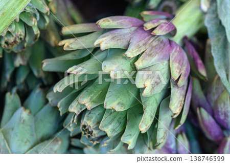 Artichokes gathered at a vibrant farmer's market bask in the glow of the morning sun, showcasing their rich hues and unique textures Artichokes gathered at a vibrant farmer's market bask in the glow of the morning sun, showcasing their rich hues and unique textures 138746599