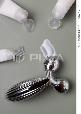 Metal facial roller with moisturizing skincare cream and cosmetic jar on neutral background, beauty treatment concept 138747080