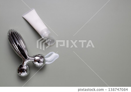Metal facial roller with moisturizing skincare cream and cosmetic jar on neutral background, beauty treatment concept Metal facial roller with moisturizing skincare cream and cosmetic jar on neutral background, beauty treatment concept 138747084