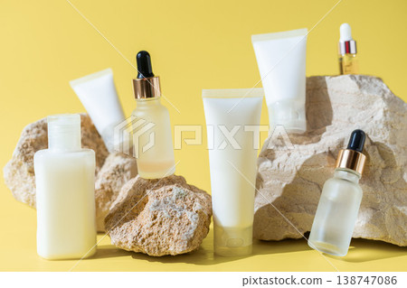 Skincare cosmetic products set with serum bottles, lotion tubes and spray bottle on natural stones with yellow background, beauty product concept Skincare cosmetic products set with serum bottles, lotion tubes and spray bottle on natural stones with yellow background, beauty product concept 138747086